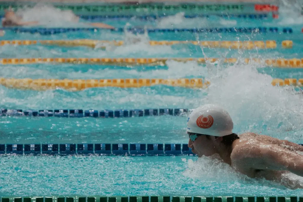 Zawodnik w czepku płynie motylkiem na torze basenu olimpijskiego.